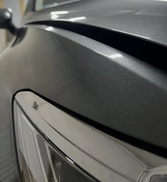 Górna krawędź przedniego błotnika szarego auta przy masce, widok wzdłuż linii nadwozia - kontrola linii po wyciąganiu wgniotki