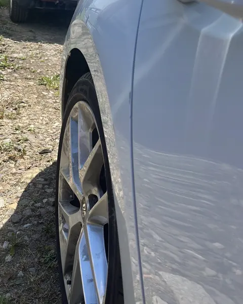 Fale w odbiciu na przednim błotniku srebrnego auta za kołem, ślad wgniecenia przy drzwiach - wgniecenie parkingowe do wyciągnięcia
